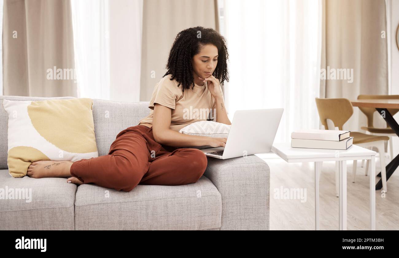 Détendez-vous, un ordinateur portable et une femme sur un canapé dans un salon pour les actualités, les médias sociaux ou la diffusion en continu dans sa maison. Femme noire, canapé et recherche en ligne pour l'éducation Banque D'Images