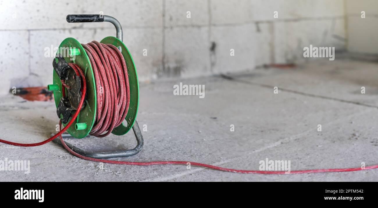 Tambour de rallonge de cordon d'alimentation rouge et vert sur le sol du chantier, détail de gros plan avec espace vide pour le texte du côté droit Banque D'Images