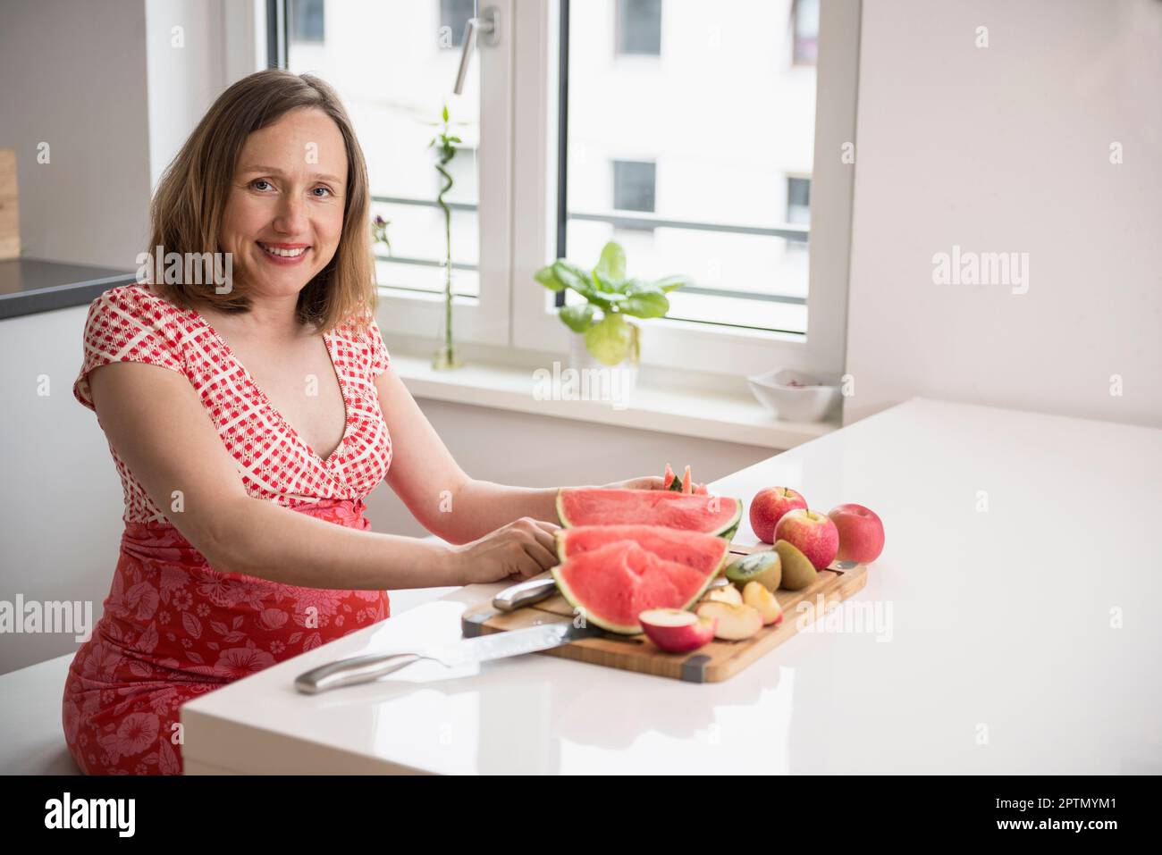 Femme enceinte coupant des tranches de pastèque dans la cuisine, Munich, Bavière, Allemagne Banque D'Images