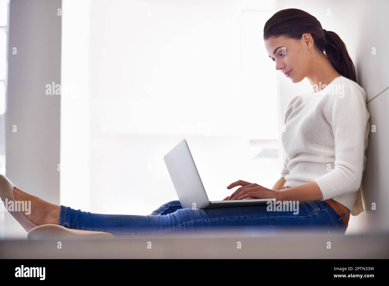 Seulement 5 minutes de plus en ligne. Une belle jeune femme assise sur son sol et utilisant un ordinateur portable Banque D'Images