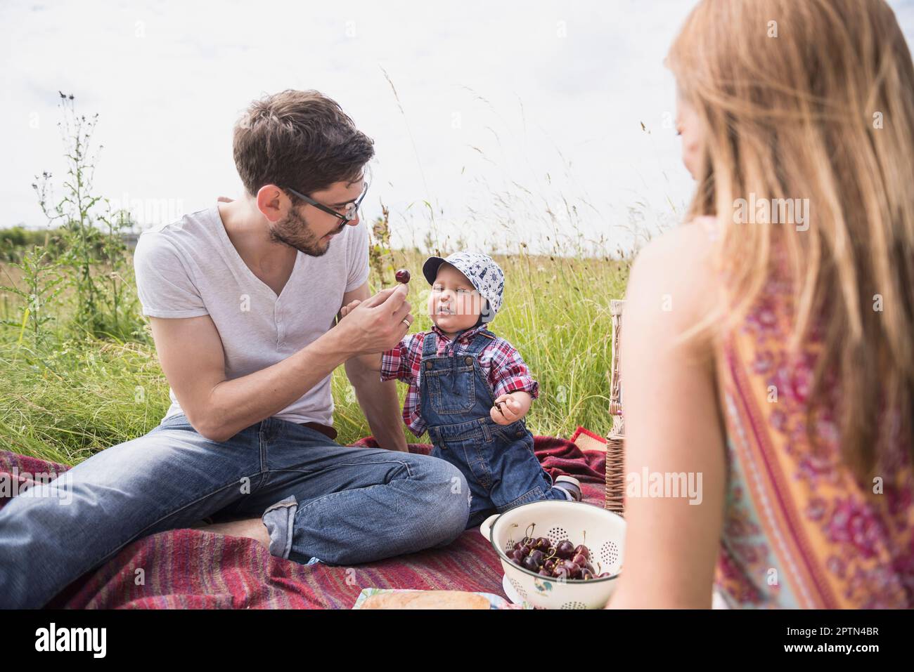 Père nourrissant des cerises à son bébé garçon sur la prairie dans la campagne, Bavière, Allemagne Banque D'Images