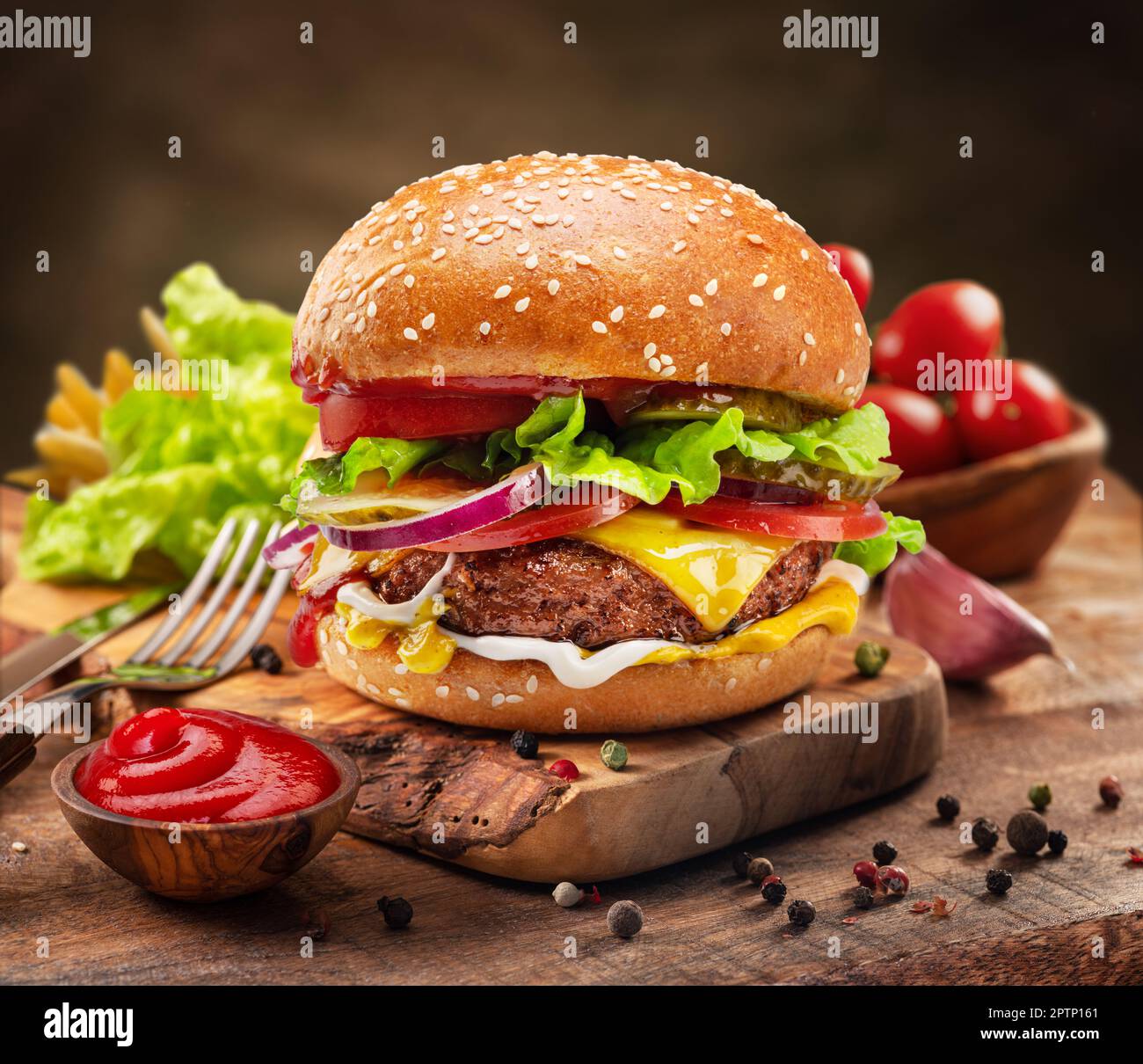 Savoureux cheeseburger ou hamburger sur plateau en bois, épices et légumes à proximité. Banque D'Images