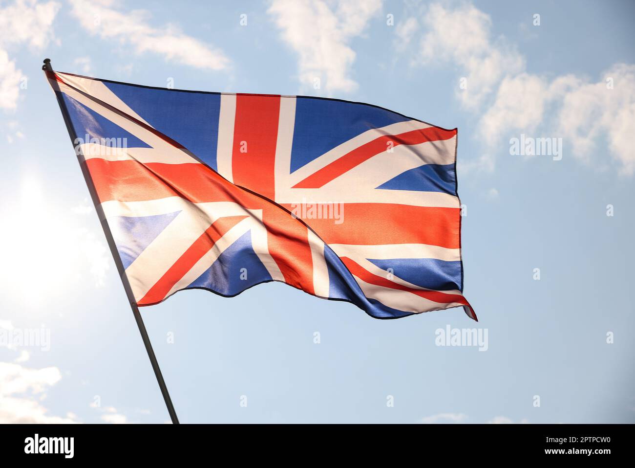 Royaume-Uni drapeau national de Grande-Bretagne volant et en agitant dans le vent, rétroéclairé dans l'heure d'or avant le coucher du soleil, sur ciel bleu ciel nuageux, symbole du patriotisme britannique Banque D'Images