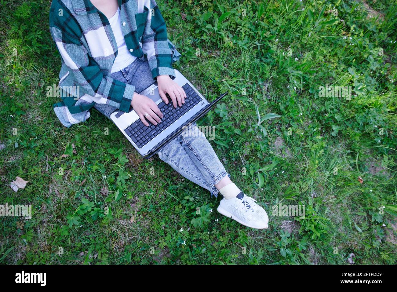 Vue de dessus d'une femme assise au parc sur l'herbe verte avec ordinateur portable, ordinateur portable et smartphone, mains sur le clavier. Étudiant étudiant étudiant en plein air. Banque D'Images