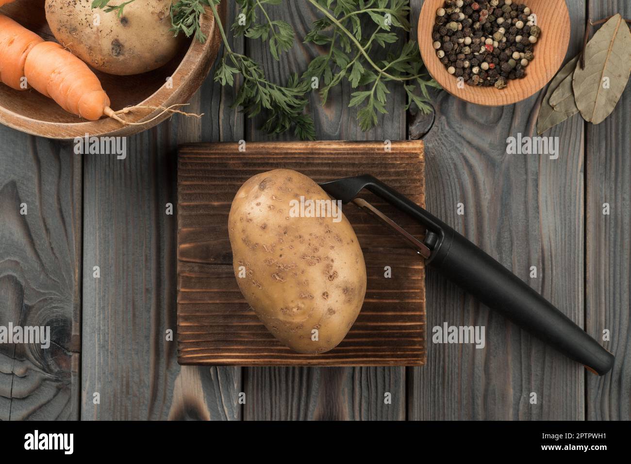 Éplucher la pomme de terre jaune avec un éplucheur de légumes. Vue de la  mise à plat. Pommes de terre fraîches non pelées. Peler la planche en bois  de la cuisine. Préparez