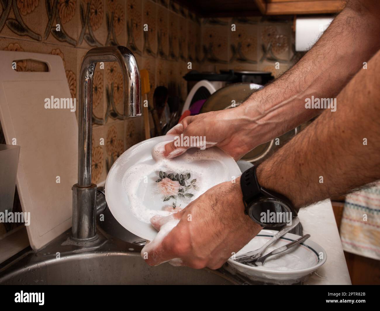 Les hommes lavent la vaisselle avec de la mousse détergente dans un ancien évier de cuisine tout en maintenant le robinet fermé. Économiser de l'eau sur les tâches ménagères Banque D'Images