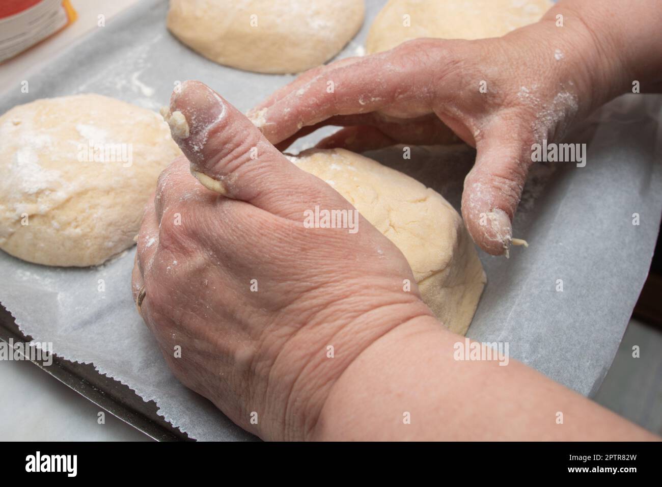 Le processus de mise en forme de la pâte à pain à la maison. Gros plan des mains des femmes préparant les petits pains sur une plaque avant qu'ils ne passent au four. Concept de fabrication du pain Banque D'Images