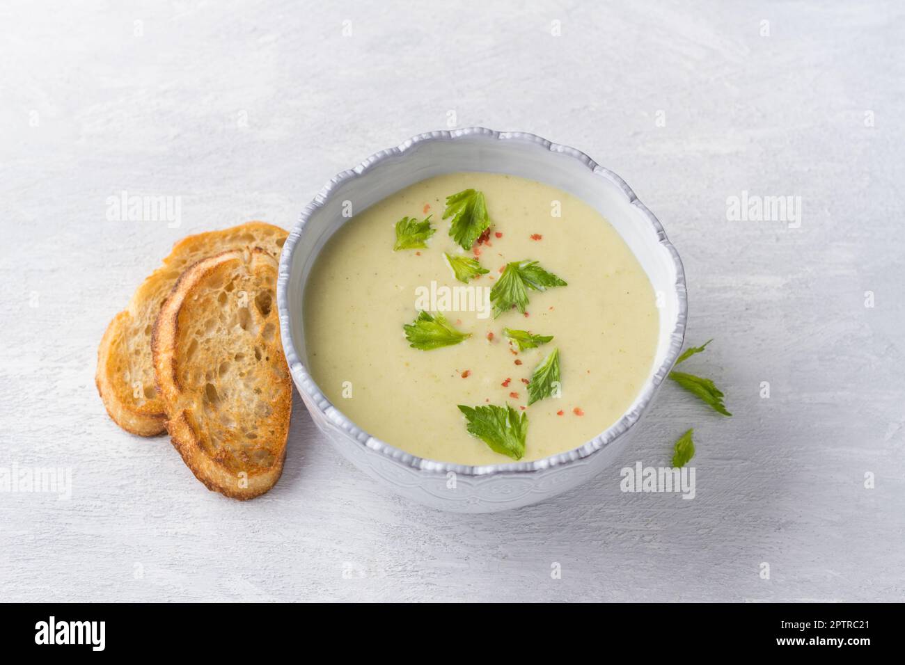 Soupe crème de céleri à branches avec crème, garni de feuilles de céleri, poivre rose et servi avec des toasts croustillants sur fond gris clair, vue du dessus Banque D'Images