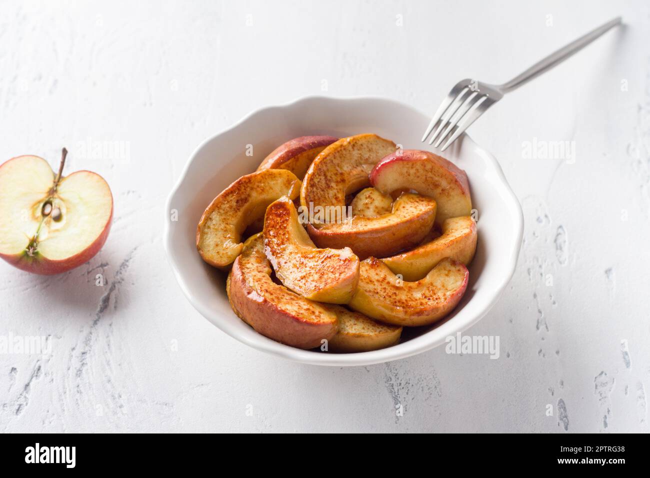 Un bol blanc de tranches de pomme cuites à la cannelle sur fond bleu clair. Délicieux dessert vegan maison Banque D'Images