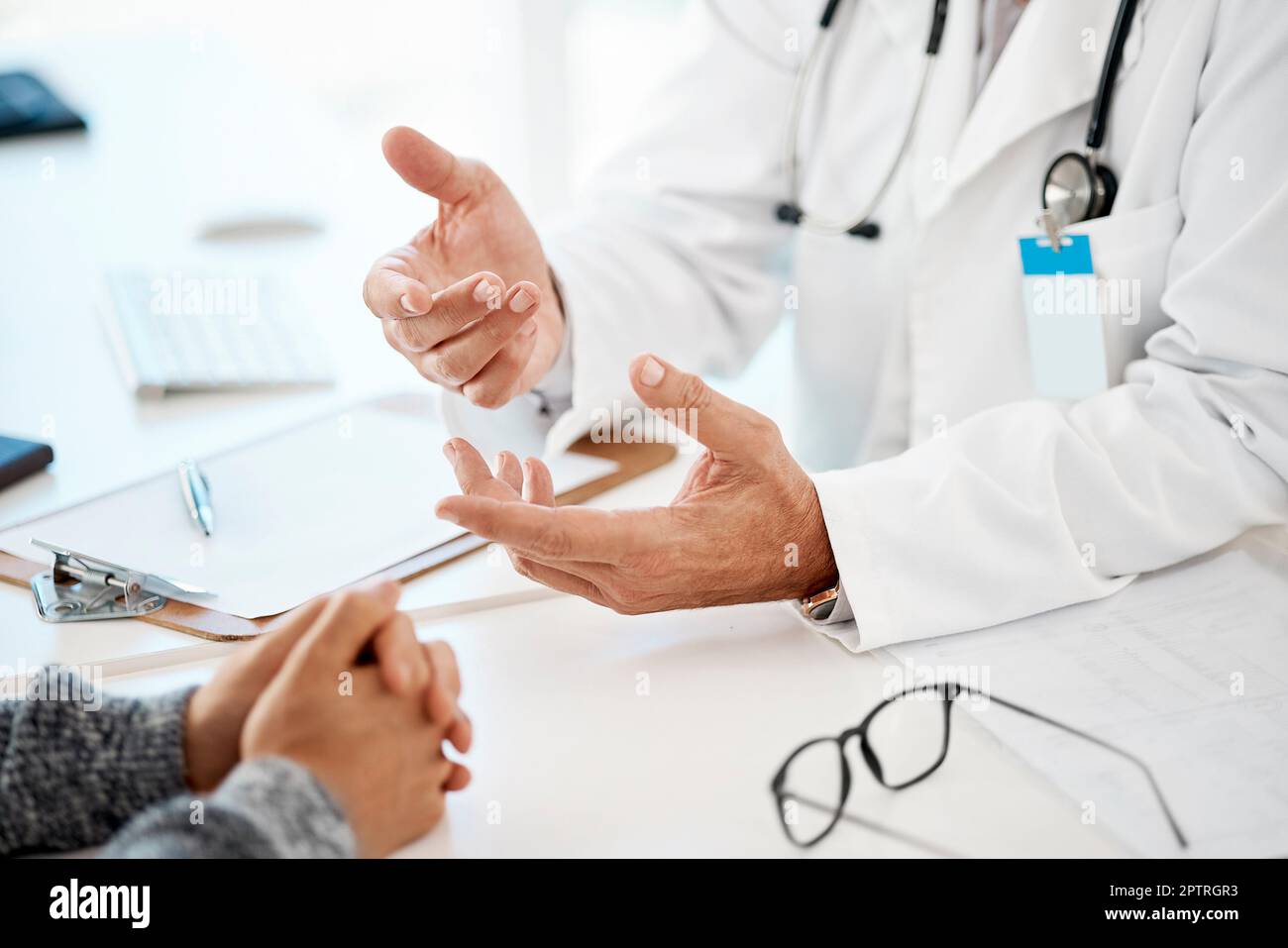 Au-dessus du gros plan des mains lors d'une consultation entre un homme caucasien médecin et un homme patient à une table dans la clinique. Patient de race mixte avec main clastée Banque D'Images