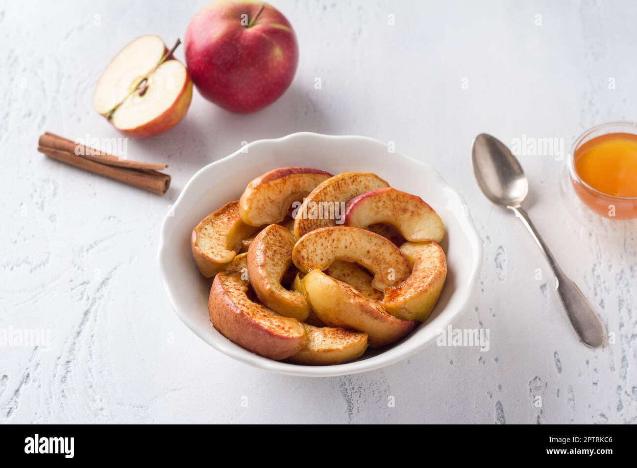 Un bol blanc de tranches de pomme cuites à la cannelle sur fond bleu clair. Délicieux dessert vegan maison Banque D'Images
