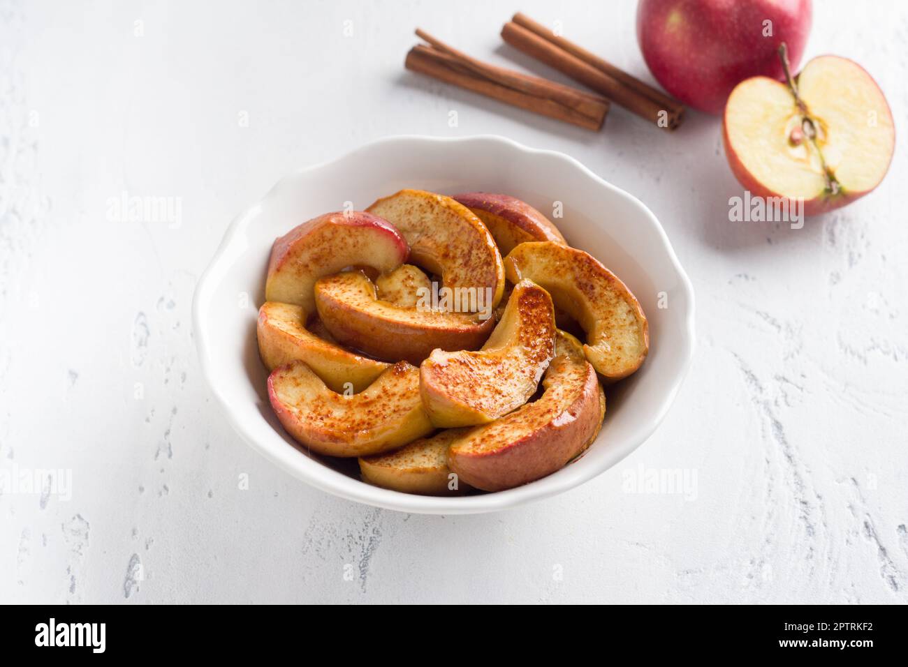 Un bol blanc de tranches de pomme cuites à la cannelle sur fond bleu clair. Délicieux dessert vegan maison Banque D'Images