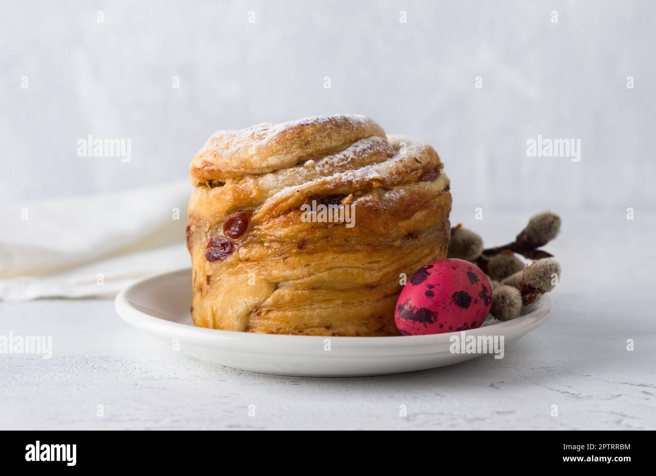 Gâteau de Pâques Kraffin aux noix et aux fruits secs, arrosé de sucre en poudre, décoré d'un œuf peint et de branches de saule sur un dos bleu clair Banque D'Images