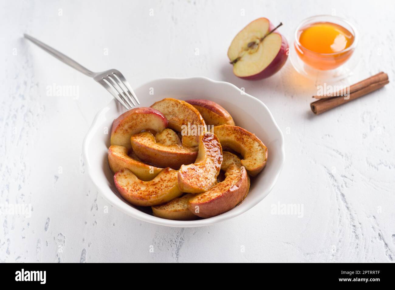 Un bol blanc de tranches de pomme cuites à la cannelle sur fond bleu clair. Délicieux dessert vegan maison Banque D'Images