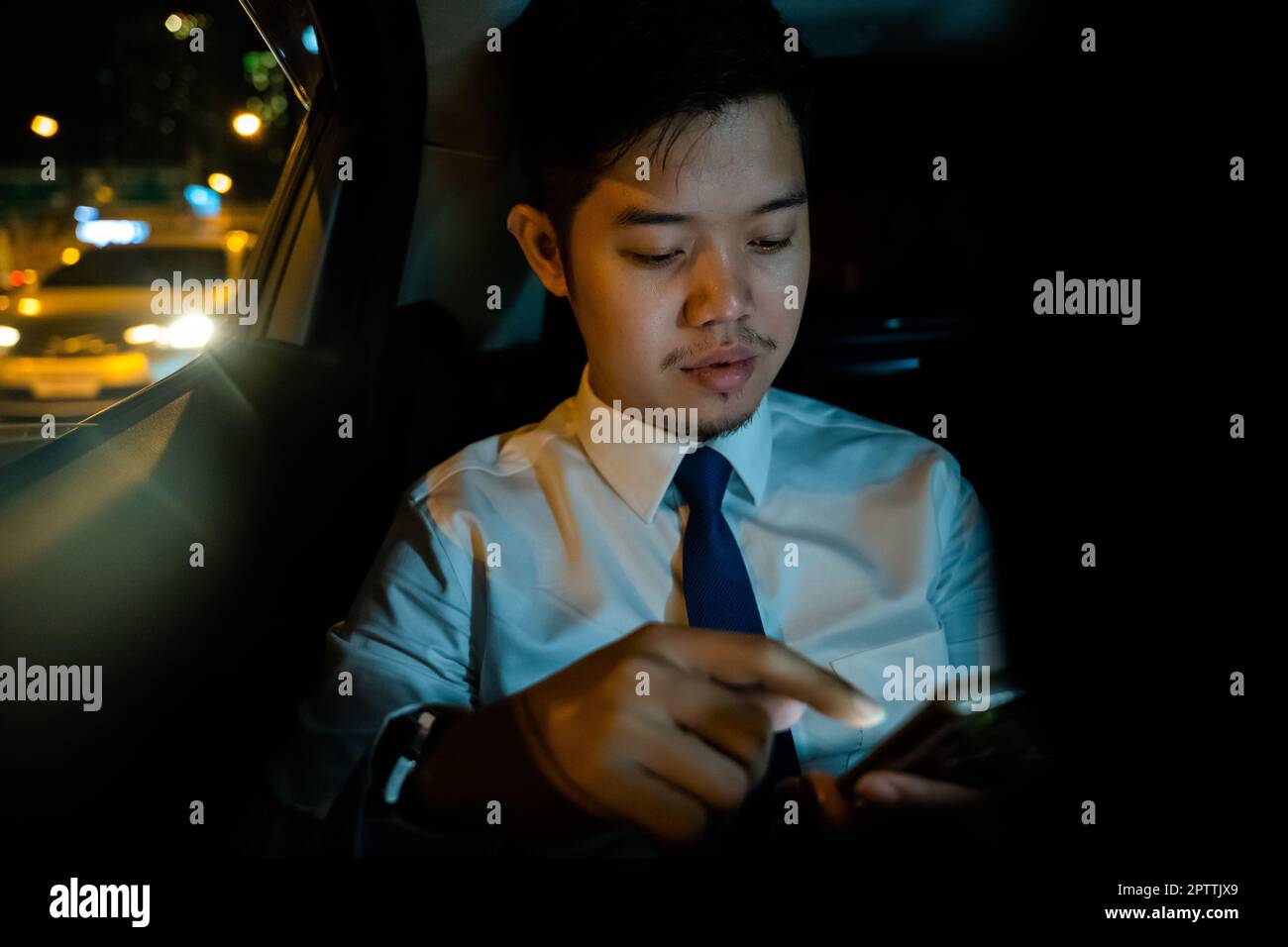 Un beau jeune homme asiatique en taxi travaille tard dans la nuit assis derrière la banquette et travaille toujours avec un téléphone portable dans la rue, homme d'affaires utilisant un smartphone dans Banque D'Images