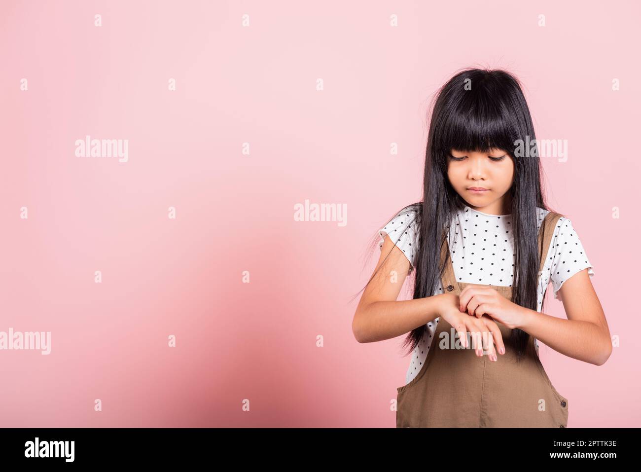 Petit enfant asiatique de 10 ans qui se gratte la main arrière de la piqûre de moustique au studio de tir isolé sur fond rose, dermatite de fille d'enfant et scabi Banque D'Images