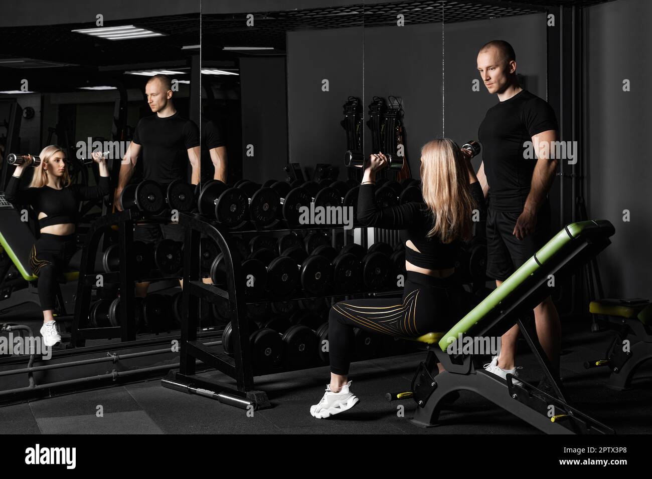 Un instructeur de fitness organise un entraînement personnel pour une fille avec un haltère devant le miroir Banque D'Images