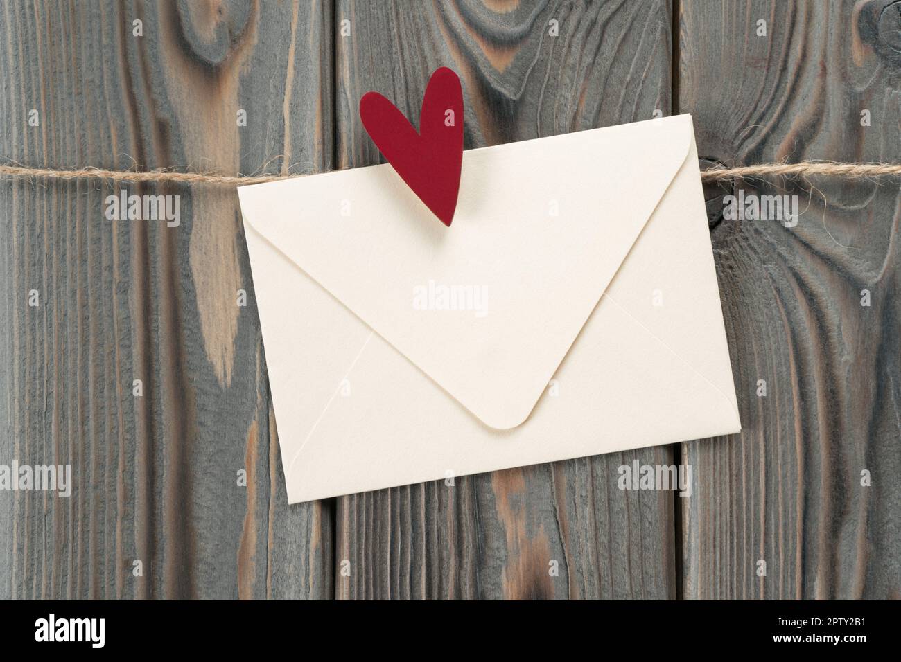 Jolie enveloppe en papier blanc fait main avec coeur rouge comme timbre,  accrochée sur corde sur fond de bois sombre. Secret présent et envoyer des  sentiments sur saint Valen Photo Stock -