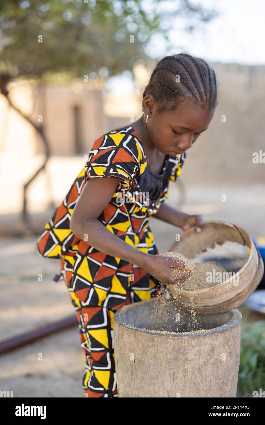 Une fillette tamise le grain de mil tout en l'estampant dans la farine dans la région de Ségou, au Mali, en Afrique de l'Ouest. 2022 Mali sécheresse et crise de la faim. Banque D'Images