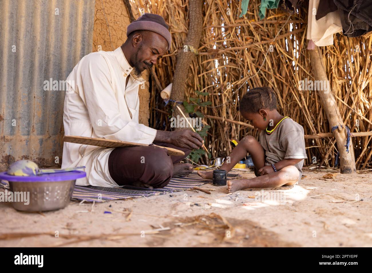Un homme pratique la calligraphie islamique à la maison avec son enfant dans la région de Ségou, Mali, Afrique de l'Ouest. 2022 Mali sécheresse et crise de la faim. Banque D'Images