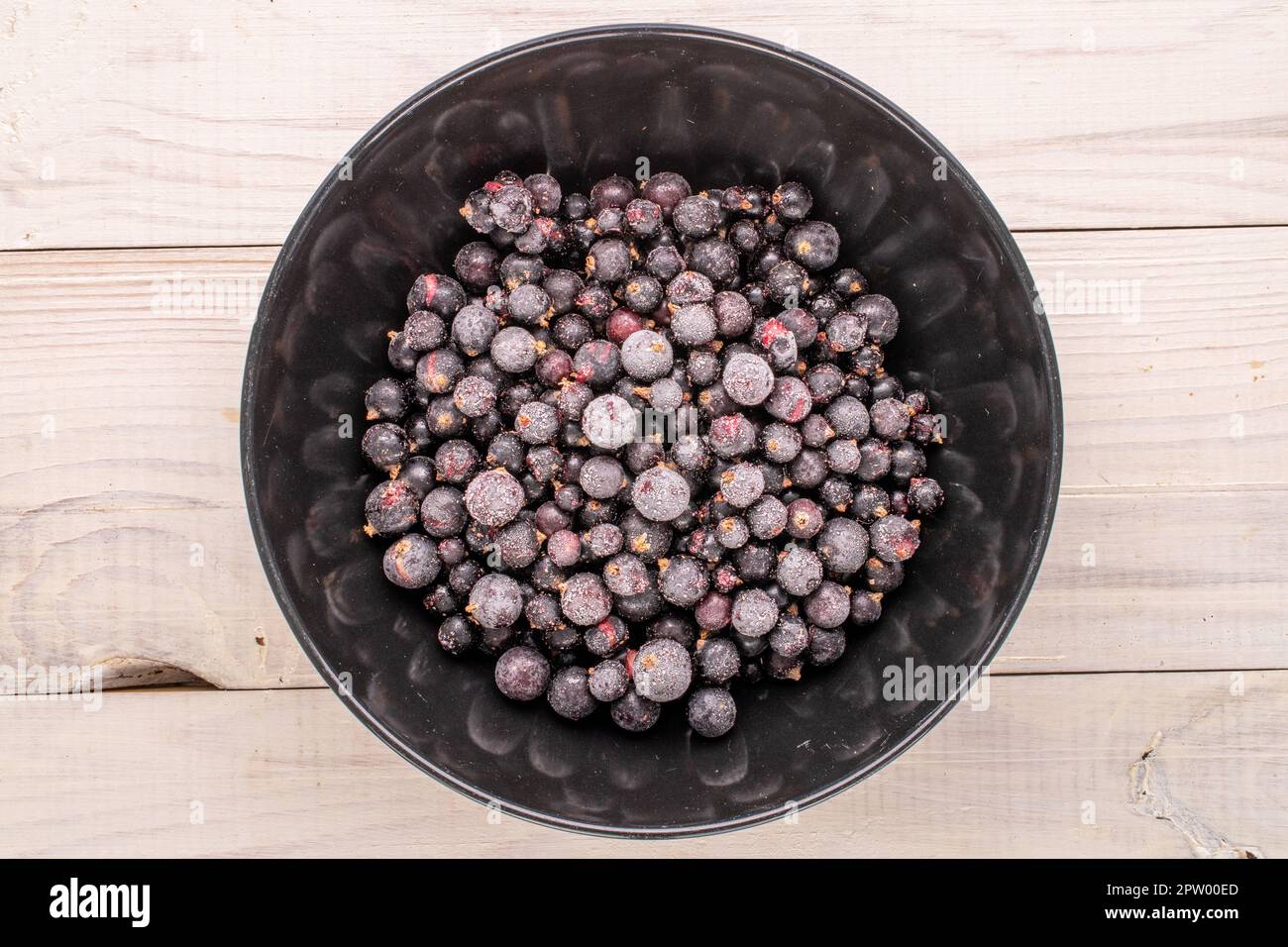Cassis surgelé avec plaque noire sur table en bois, macro, vue de dessus. Banque D'Images