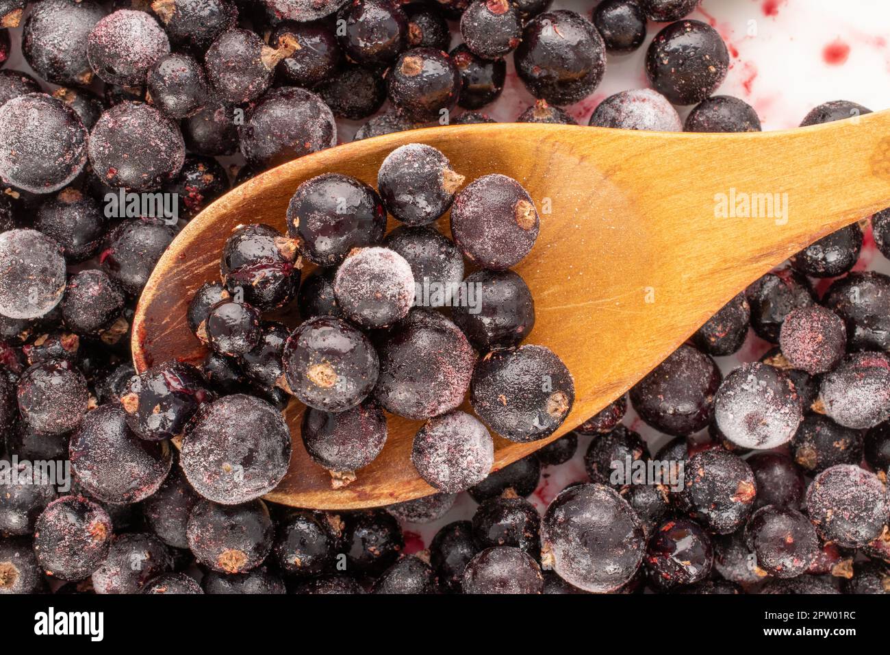 Cassis surgelé avec cuillère en bois, macro, vue de dessus. Banque D'Images