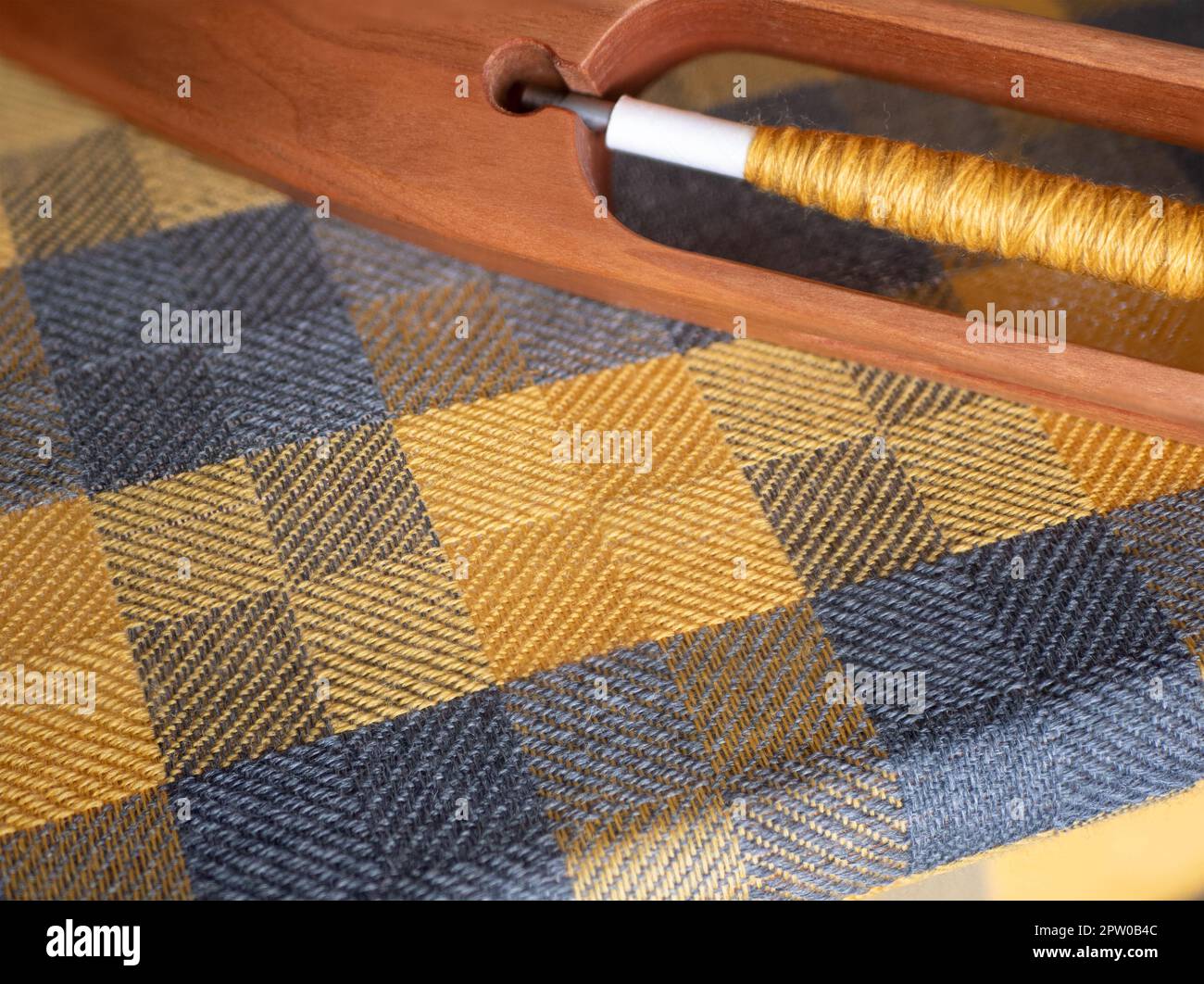 Tissu tissé à carreaux jaune et gris sur un métier à main avec une navette de bateau en bois, mise au point sélective. Détail du tissage Banque D'Images