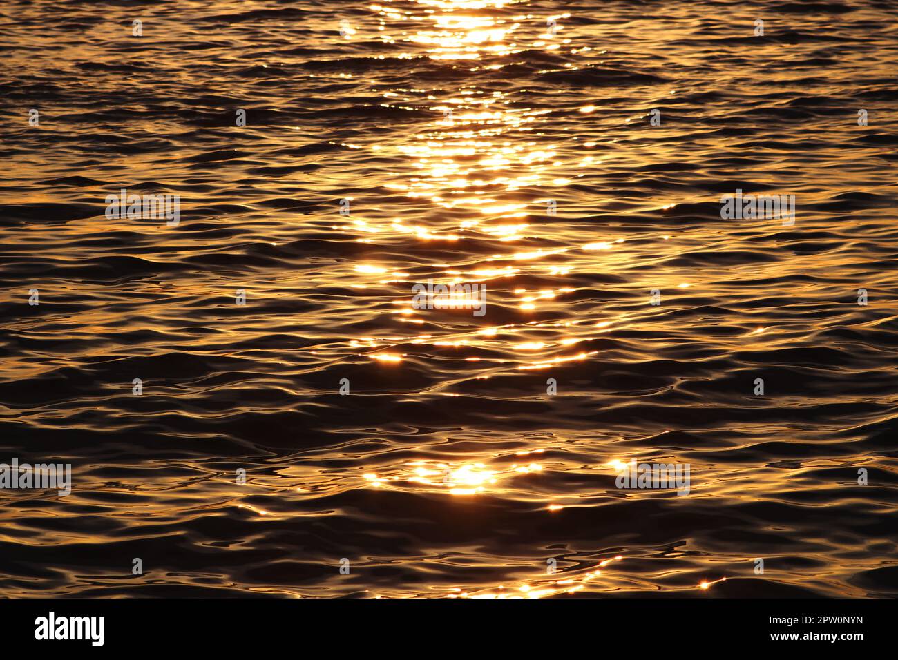 Coucher de soleil doré sur la mer orange vif coloré, ligne jaune des derniers rayons du soleil, reflet du soleil sur l'eau sombre calme avec peu d'ondulation de brise, texture de l'eau. Banque D'Images