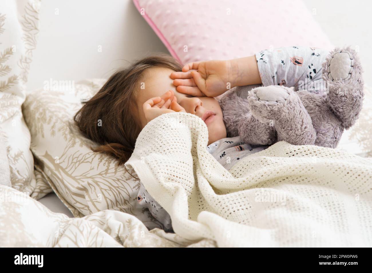 Triste, déçu, pleurant enfant fille frottant les yeux, tenant le jouet bourré, allongé dans un lit blanc doux avec des oreillers le matin. Blessé et enfant de la famille abu Banque D'Images