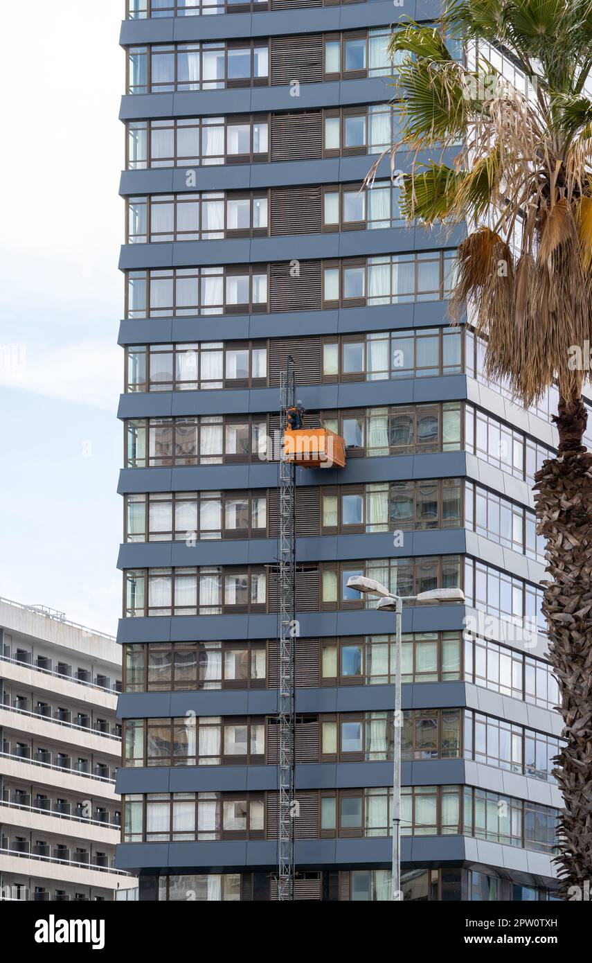 Les techniciens d'entretien sur un berceau suspendu ou une plate-forme élévatrice effectuent des travaux de réparation sur la façade d'un immeuble de bureaux et d'une fenêtre modernes à plusieurs étages Banque D'Images