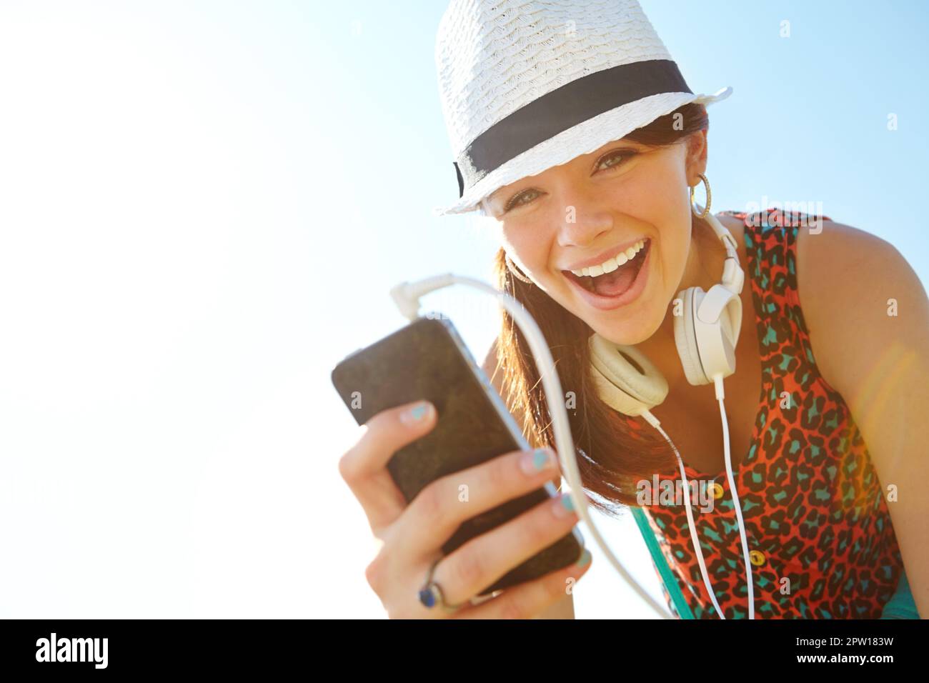 Découvrez le son de l'été. Une adolescente heureuse souriant tout en tenant un smartphone avec son casque Banque D'Images