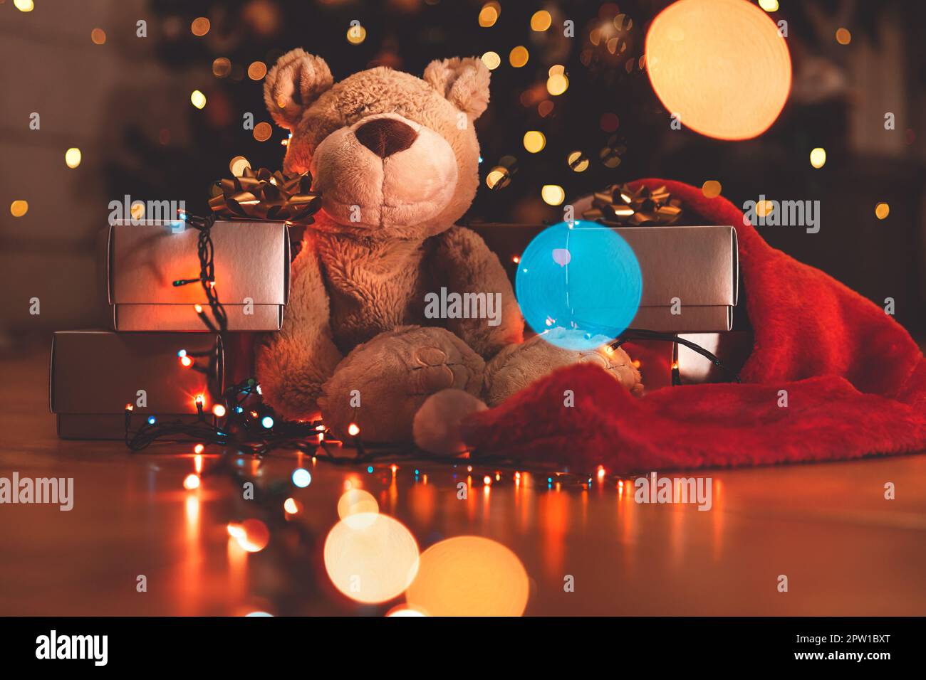 Joli ours avec des boîtes cadeau argentées sous un magnifique sapin de