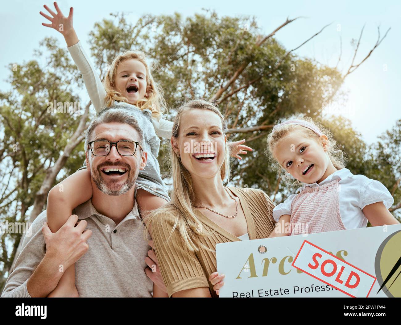 Portrait d'une famille caucasienne heureuse tenant une affiche vendue tout en déménageant et en déménageant dans une nouvelle maison. Les parents souriants et les enfants sûr prêt de propriétaire de maison pour Banque D'Images
