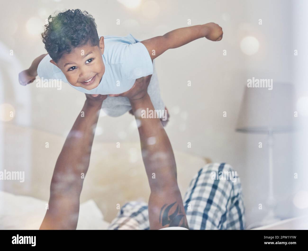 Joyeux petit garçon de course mixte volant dans les bras de pères regardant l'appareil photo dans la chambre. Papa tenant et soulevant mignon petit enfant jouant et ayant le plaisir sur b Banque D'Images