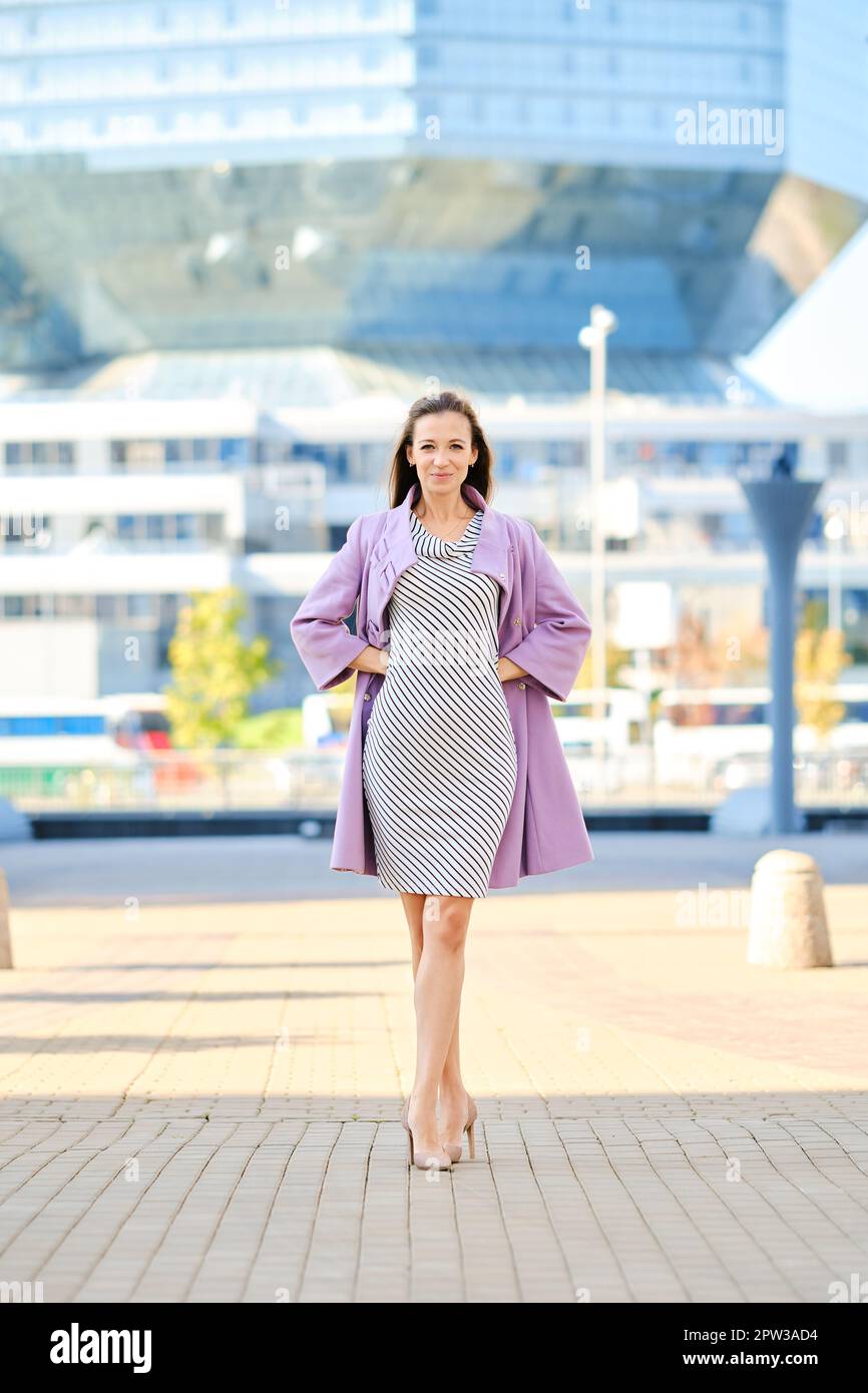 Femme tendance en manteau lilas et robe rayée posant à l'extérieur Photo  Stock - Alamy