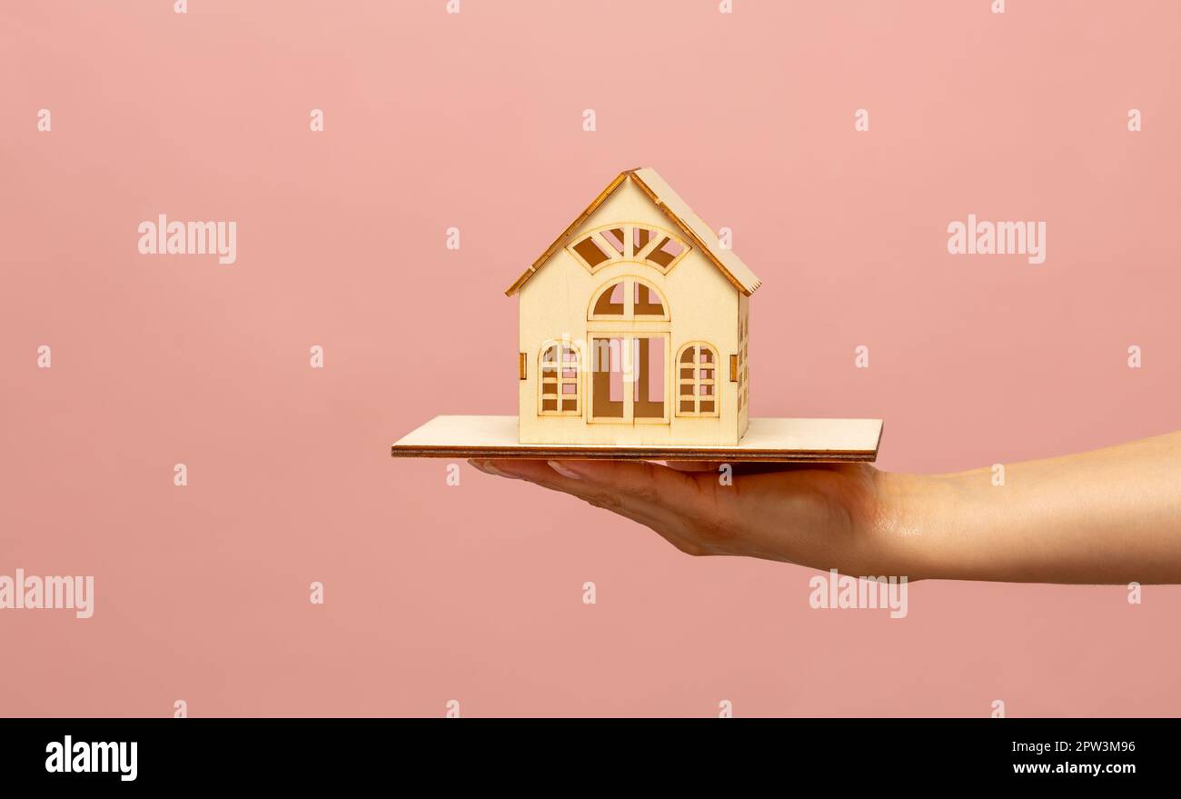 La main d'une femme tient un modèle miniature d'une maison, une maquette d'un chalet sur fond rose. Achat immobilier, nouvel immobilier, propriété, inconvénients Banque D'Images