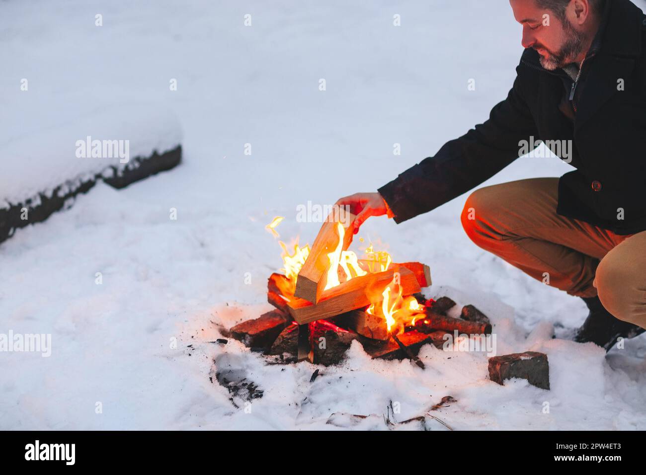 Homme mûr réchauffant ses mains avec le feu après avoir fait feu de camp au milieu de la forêt neigeuse en hiver froid soir, en utilisant la chaleur pour se sentir bien et Banque D'Images