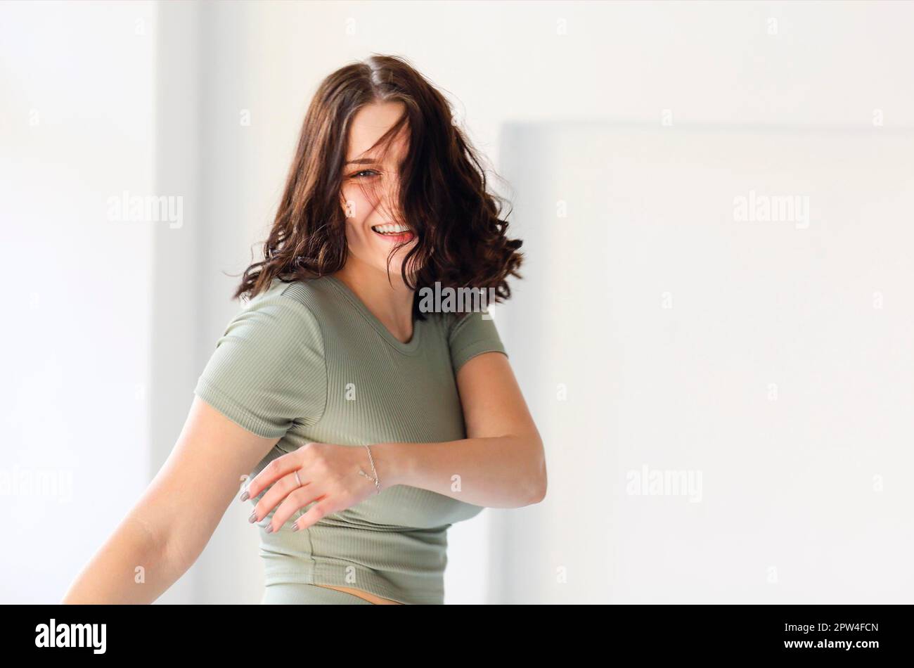 Photo en mouvement d'une jeune femme gaie, sautant ou faisant du sport en intérieur, regardant l'appareil photo en arrière tout en se déplaçant avec un large sourire, posant contre le flou Banque D'Images