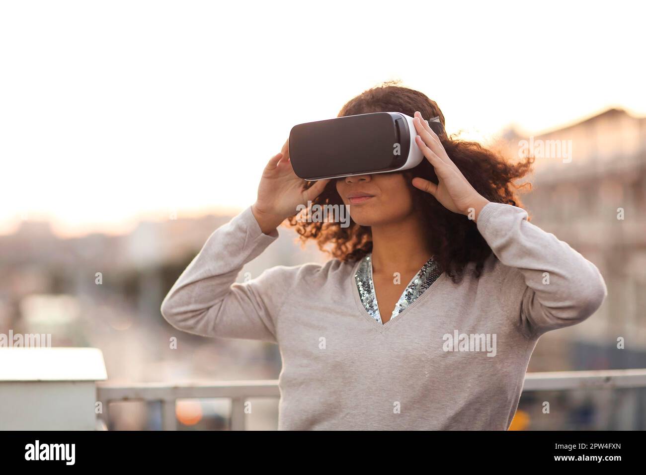 Technologie future.Jeune femme moderne de course mixte dans VR lunettes casque explorant la réalité virtuelle en plein air avec paysage urbain en arrière-plan, femme essayant Banque D'Images
