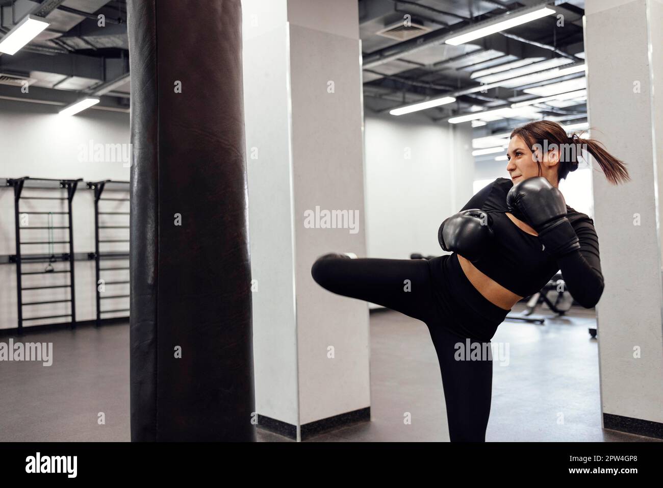 Une femme de boxe latine forte saute de coup de pied à un énorme sac de poinçonnage à la salle de fitness. Entraînement de fille athlétique Muay Thai boxe pour le culturisme et la santé Banque D'Images