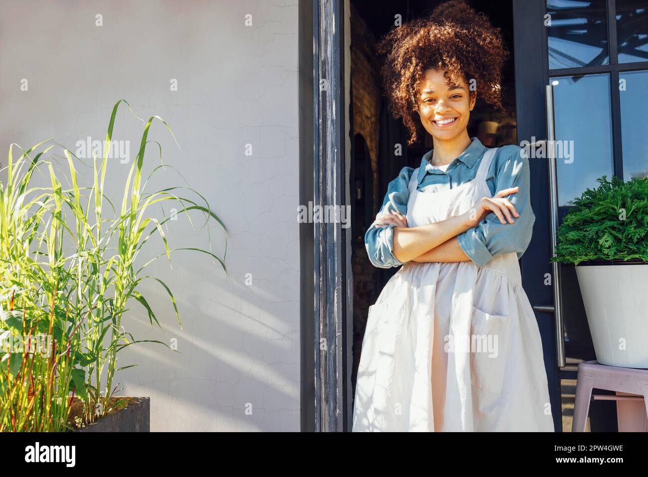 Propriétaire du café debout à l'entrée de son café. Joyeux jeune Barista jolie femme debout à la porte d'un restaurant et regardant la caméra Banque D'Images