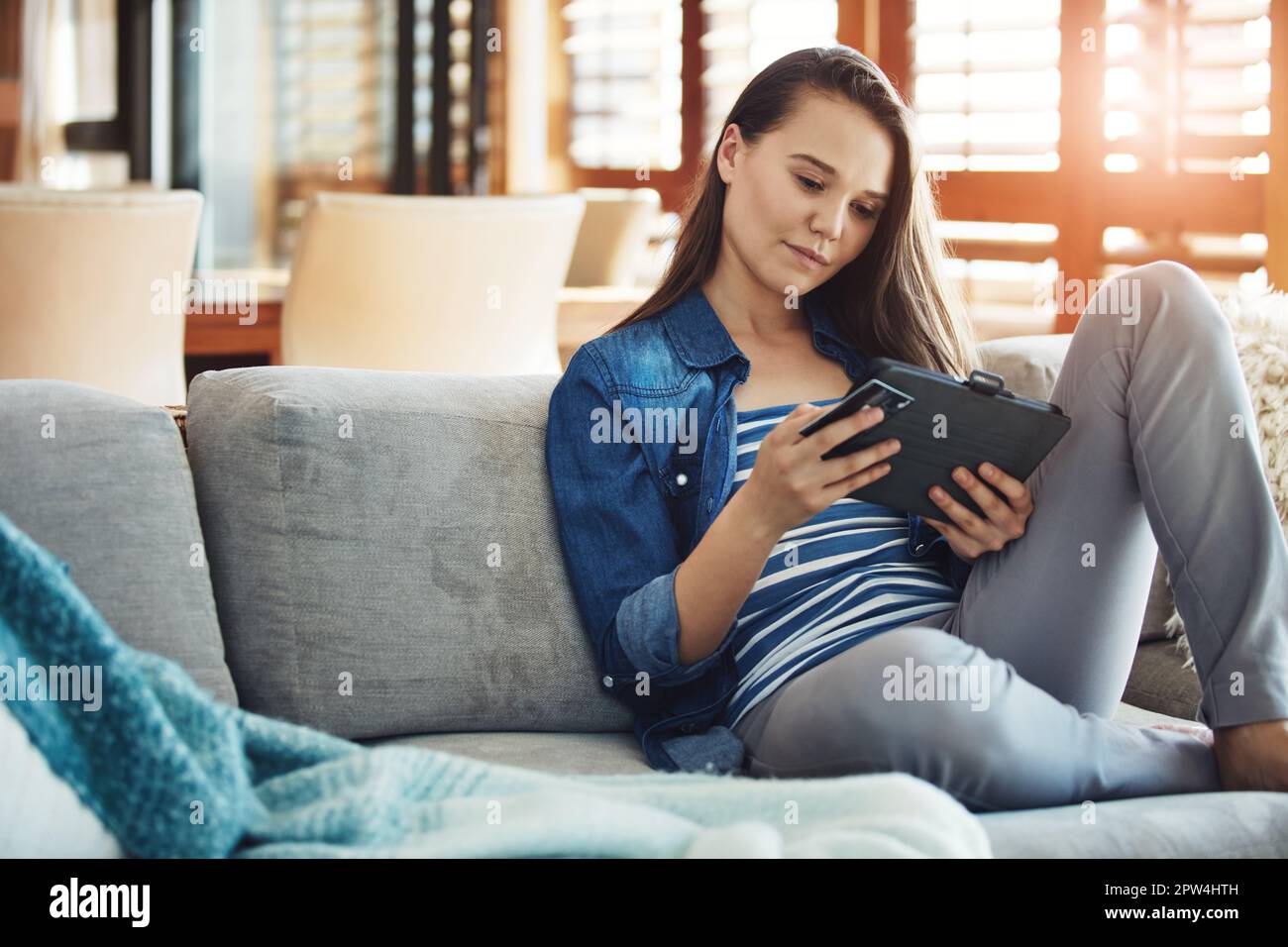 Shopping dans le confort de la maison. une jeune femme attrayante utilisant sa tablette pour faire des achats en ligne tout en se relaxant sur le canapé à la maison. Banque D'Images