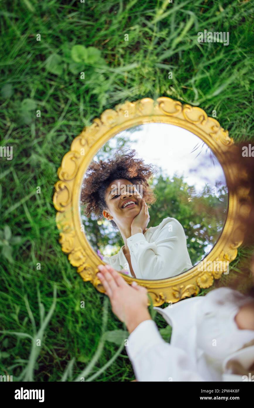 Beautifal femme de course mixte portant une robe blanche et un reflet du ciel dans un miroir rond sur l'herbe de printemps verte. Concept de la nature Banque D'Images