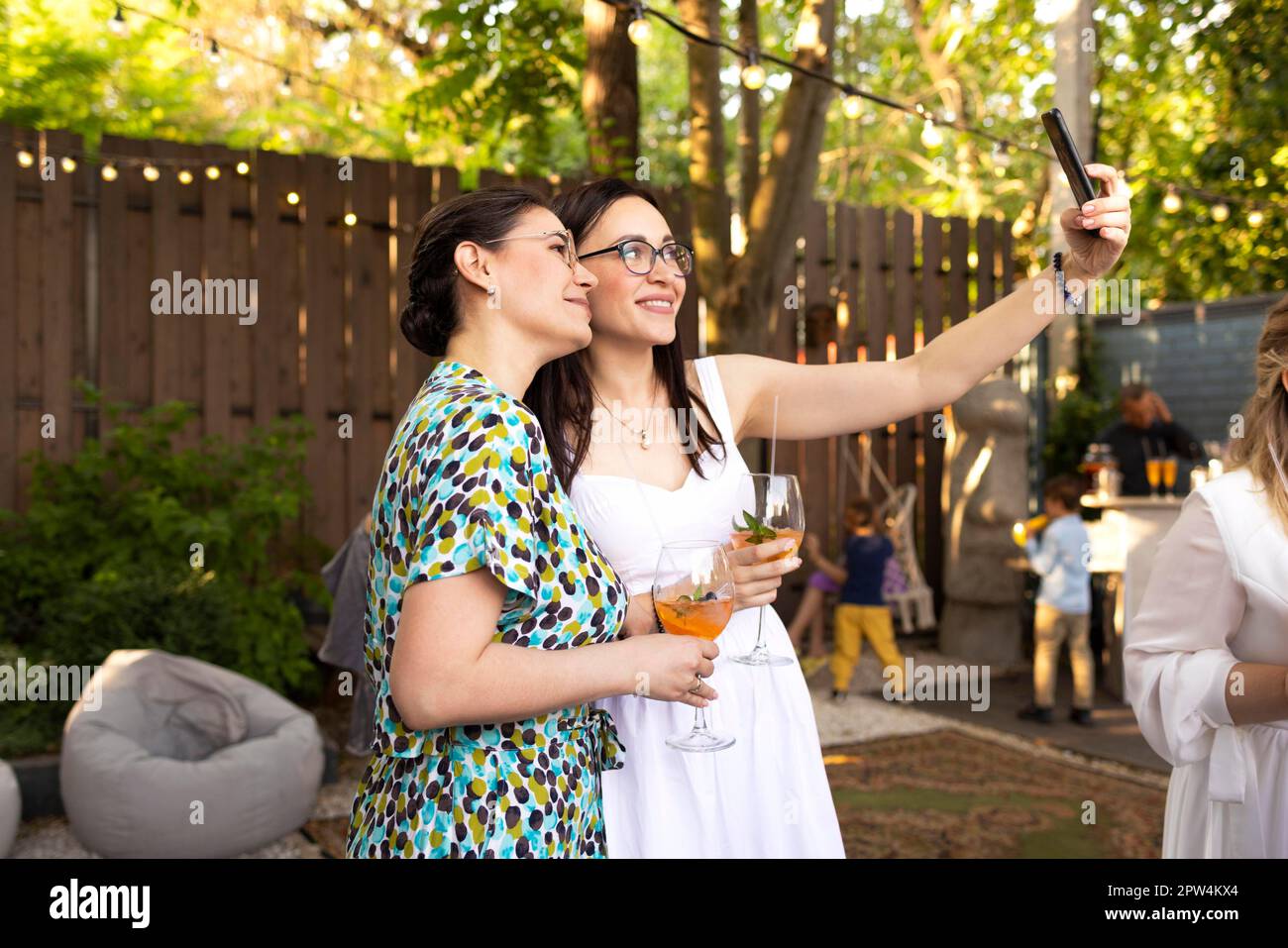 Des amies joyeuses passent du temps ensemble, une jeune femme boit un cocktail Aperol spritz lors d'une fête de mariage en plein air, faisant le selfi ensemble. Bonheur Banque D'Images