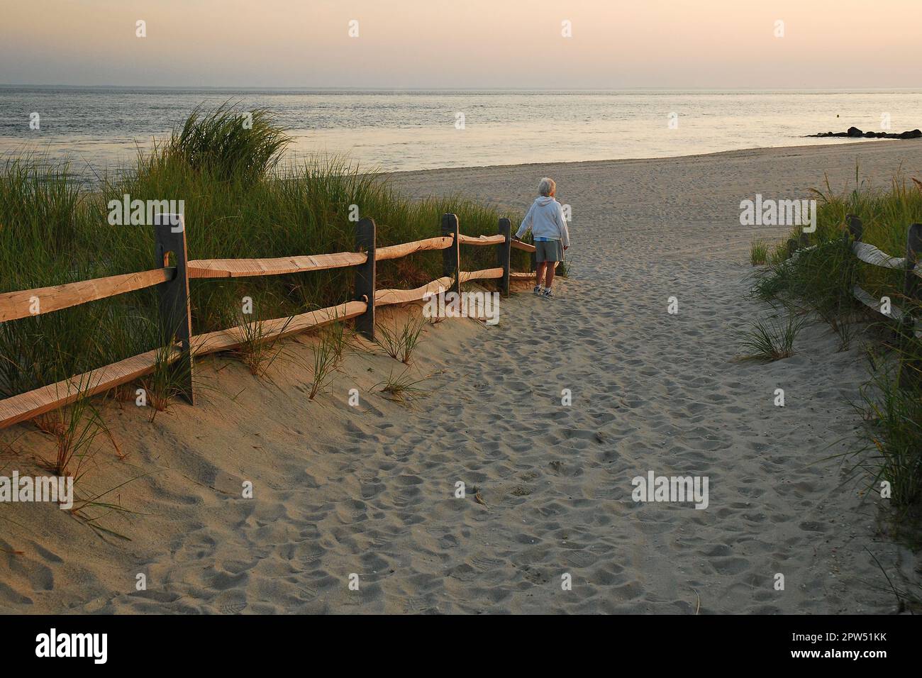 Une femme âgée marche seule le long d'un chemin à travers les dunes vers la mer au coucher du soleil Banque D'Images