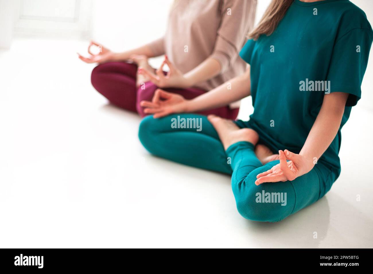 Une vue rapprochée des femmes méconnaissables dans des vêtements de sport assis avec des jambes croisées et des mains mudra sur le tapis et faisant du yoga tout en pratiquant la pleine conscience Banque D'Images