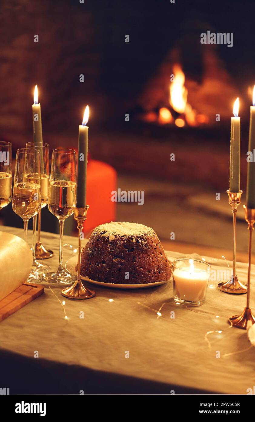 Table de dîner confortable avec gâteau de Noël fraîchement cuit, bougies allumées, lumières de Noël comme décoration et de grandes verres remplis de champagne Banque D'Images