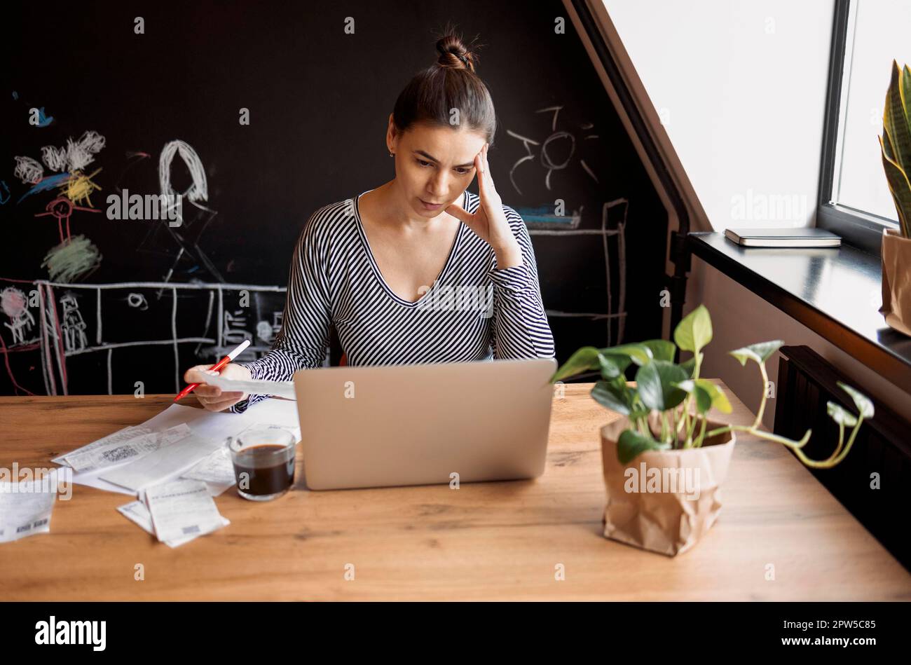 Une femme au foyer sérieuse est assise à table dans la cuisine maison pour vérifier les factures des ménages, faire des calculs sur la calculatrice, payer les services publics par le biais du système e-banking sur Banque D'Images