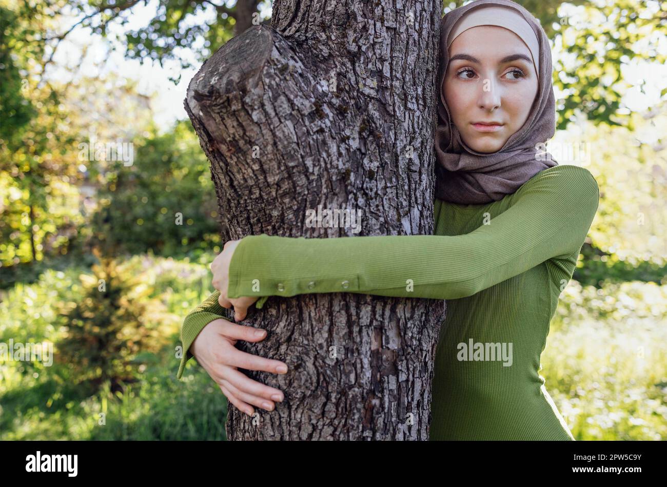 Jeune fille musulmane embrassant un arbre. Gros plan d'une jeune femme dans un hijab et de vêtements décontractés dans le parc. Protéger l'environnement et les soins Banque D'Images