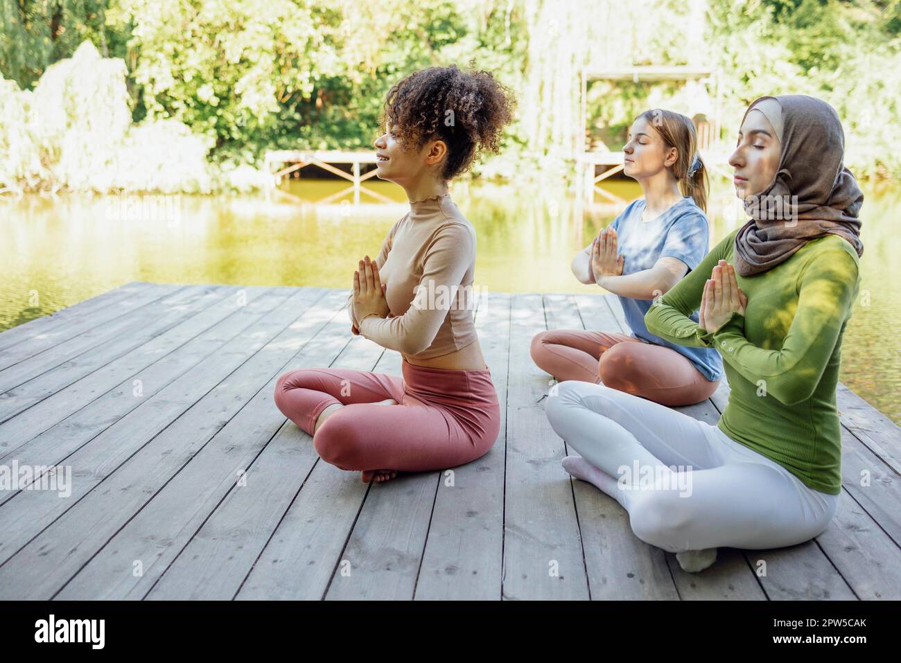 Groupe d'adolescents est engagé dans la forme physique sur la jetée au bord du lac ou de la rivière. Les jeunes filles et les filles positives vont dans le sport. Musulman dans un hijab, afro-américain Banque D'Images